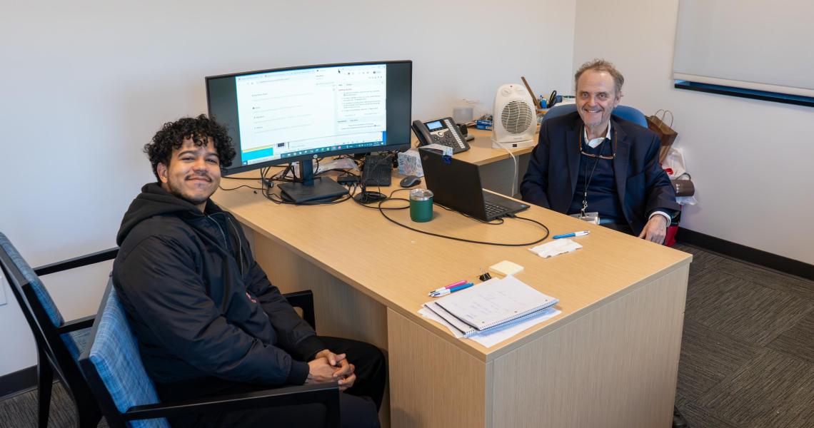 Two men sitting at office desk, smiling.