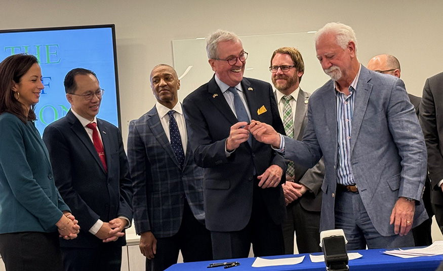 Gov. Phil Murphy smiling with NJIT staff, getting ready to sign.